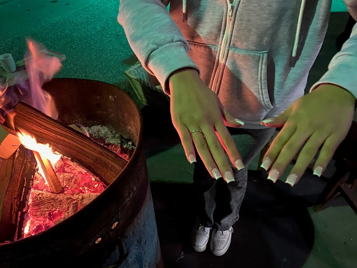 Sich mit Fingernägeln zu befassen, ist unter den Mädchen sehr beliebt. Neben einem Lagerfeuer zeigt ein Mädchen ihre schön gepflegten Fingernägel.
